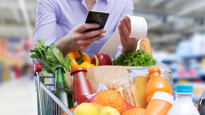 grocery store customer checking phone and receipt