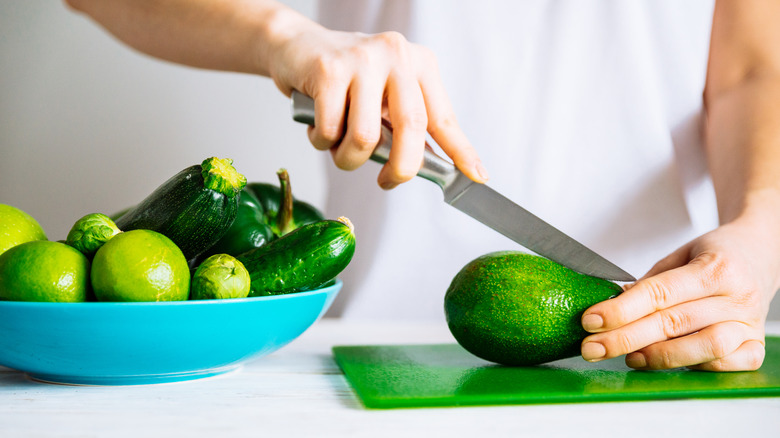 A person slices a green avocado on a cutting board