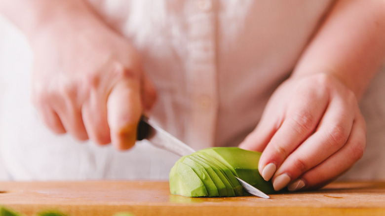 A person slices an avocado on a cutting board