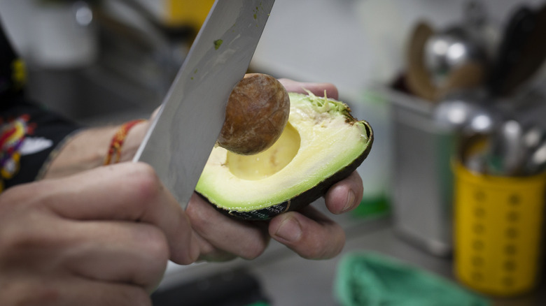 A person uses a knife to remove an avocado pit