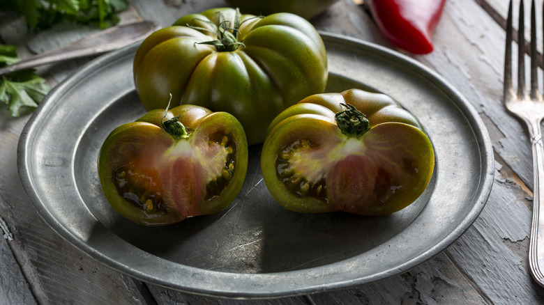 Whole green tomato and green tomato halves on a metal plate