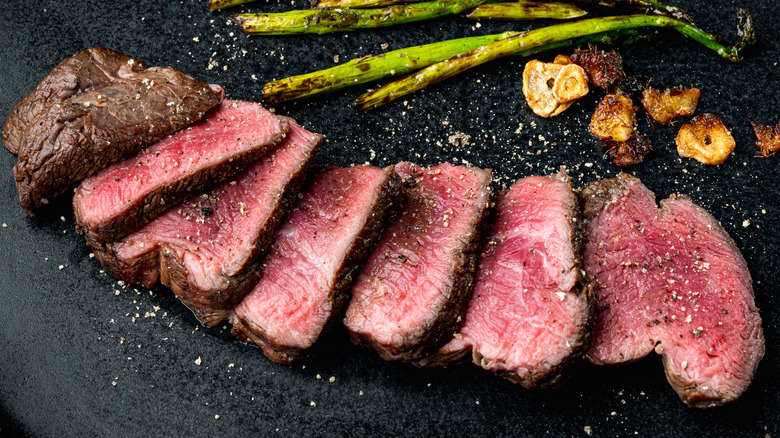 Whole filet mignon cut into slices with spices on top and asparagus