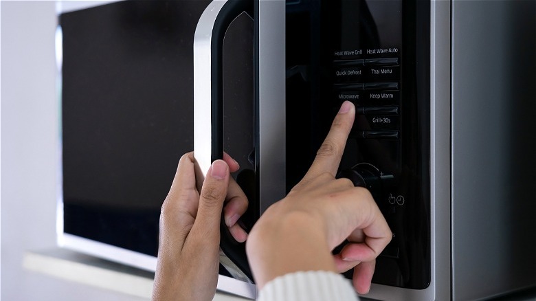 Hand pressing buttons on microwave