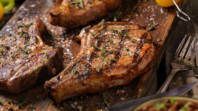 Seared pork chops sprinkled with herbs and salt on a wooden cutting board