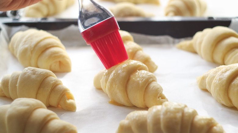 Pastry brush applying egg wash on croissant