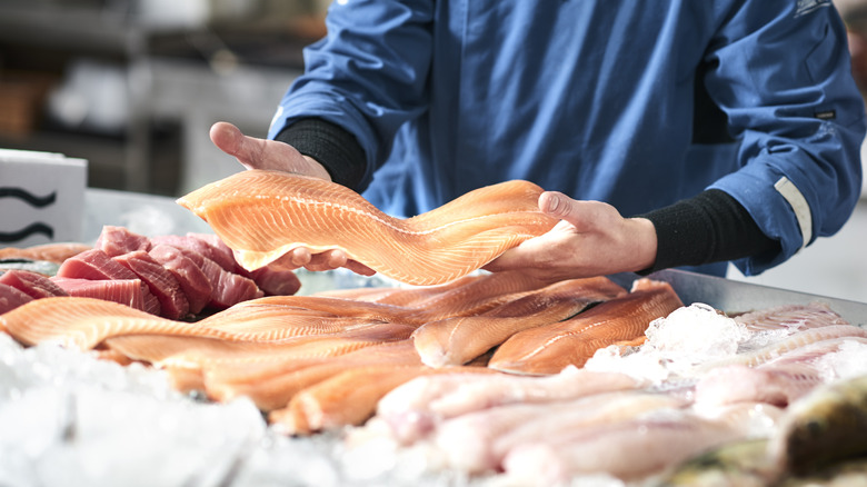 Fish monger handling side of fish over ice at fish display.