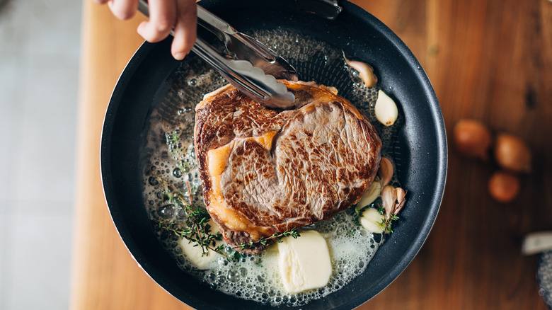 tongs flipping butter-basted steak