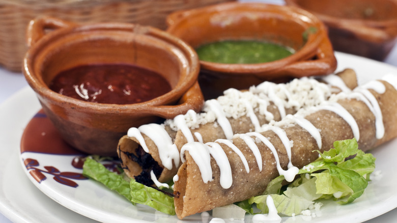 Two flautas with dipping sauce on a plate