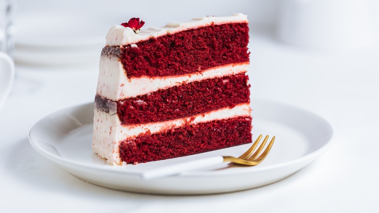 Wedge of red velvet cake with three layers and white buttercream