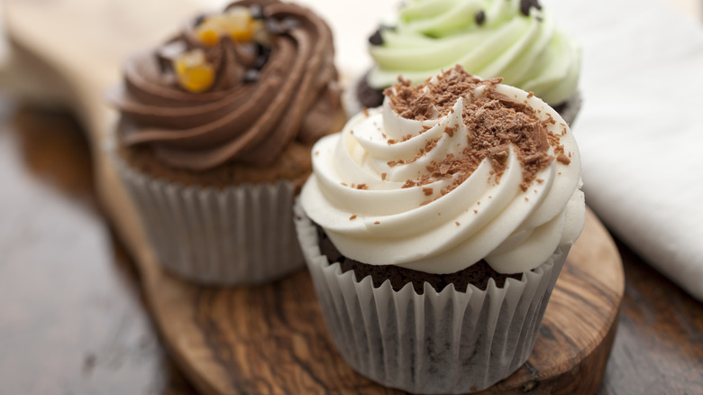 Three different flavored cupcakes grouped on a wooden board