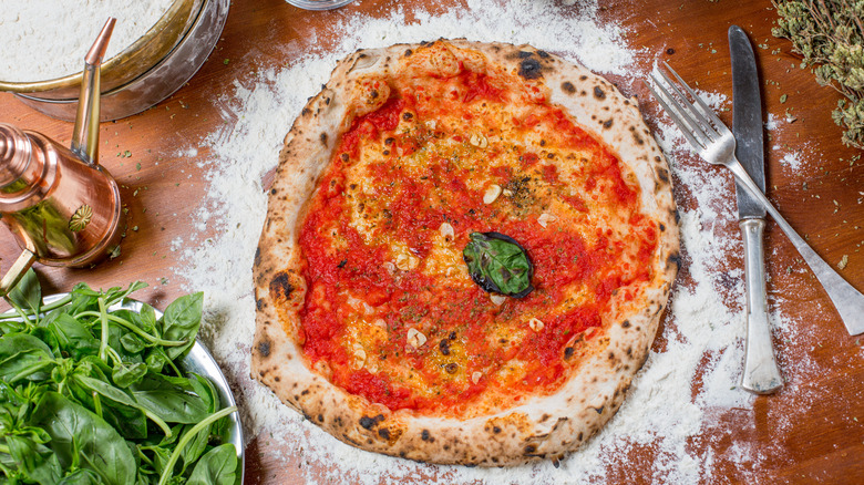 Pizza marinara and ingredients on floury countertop