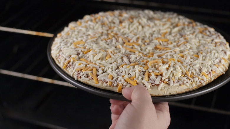 hand placing frozen pizza in oven