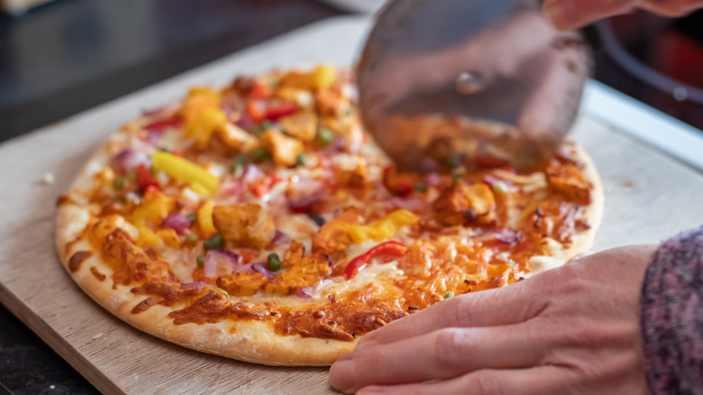 Person cutting pizza on wooden board