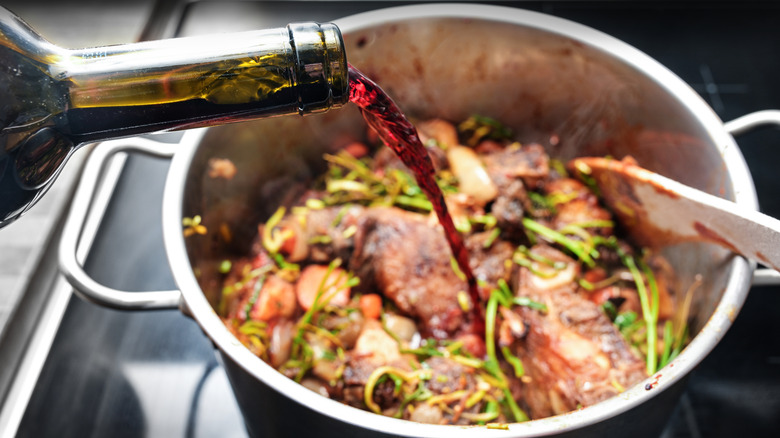 a cook pouring red wine from a bottle into a pot roast on the stove