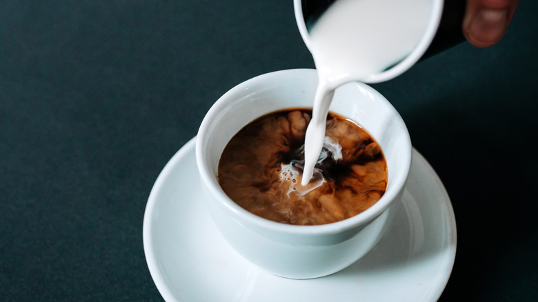 Person pouring creamer into coffee