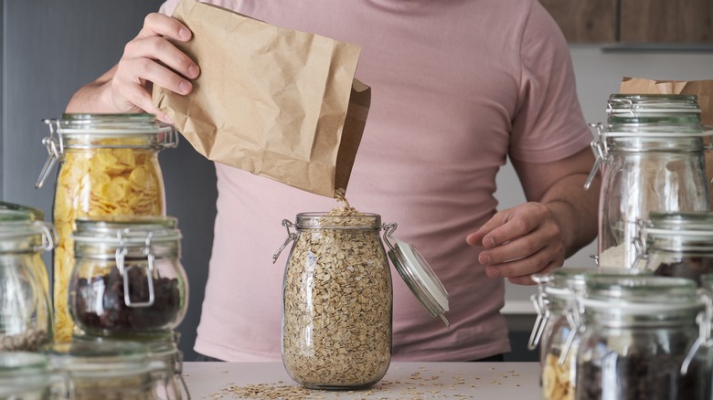 Man filling up a glass jar with dry oats 