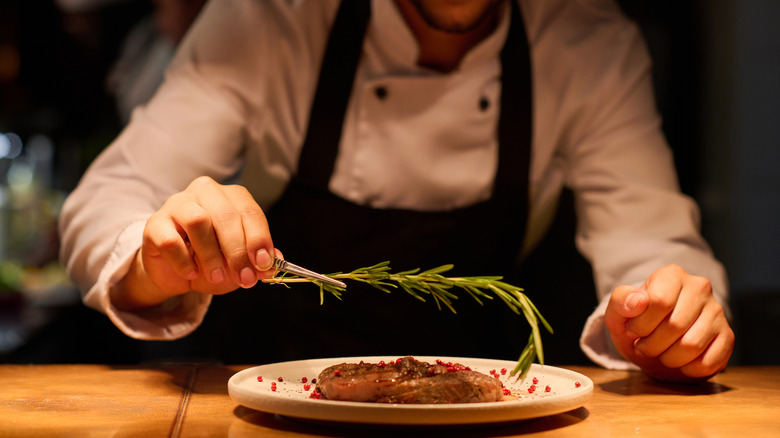 Chef placing rosemary on cooked beef on restaurant line.