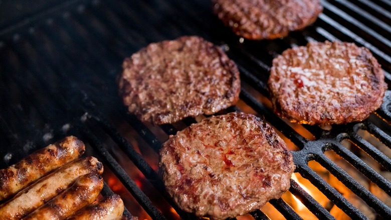 burger patties on grill above fire along with hotdogs