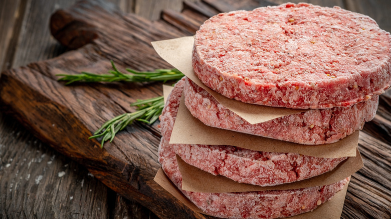 Frozen hamburger patties in stack on wooden board