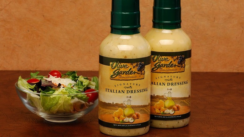 two bottles of olive garden dressing next to bowl of salad