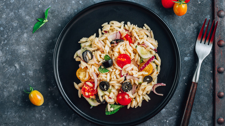 Orzo with tomatoes, olives, in black bowl