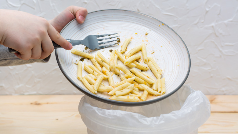 Pasta getting scraped off plate and into a bin