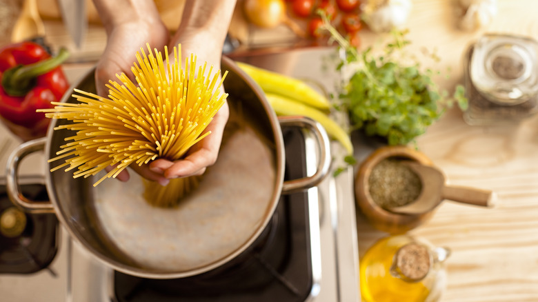 Hands putting dry spaghetti into pot on stovetop