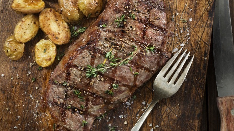 Grilled steak with a side of roasted potatoes on a wooden board.