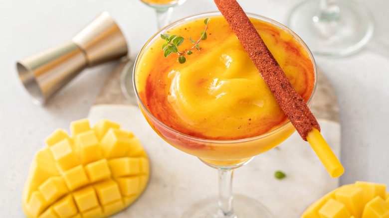 A frozen mango margarita in a margarita glass surrounded by sliced mangos.