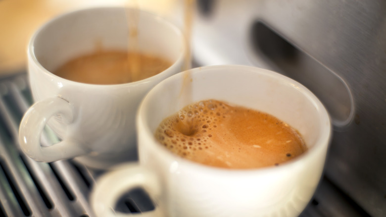 Coffee from machine pouring into two mugs