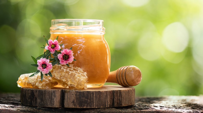 jar of honey with honeycomb and flowers