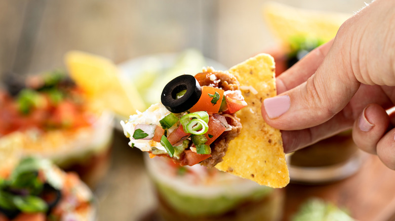 Person holding tortilla chip dipped in layered dip.