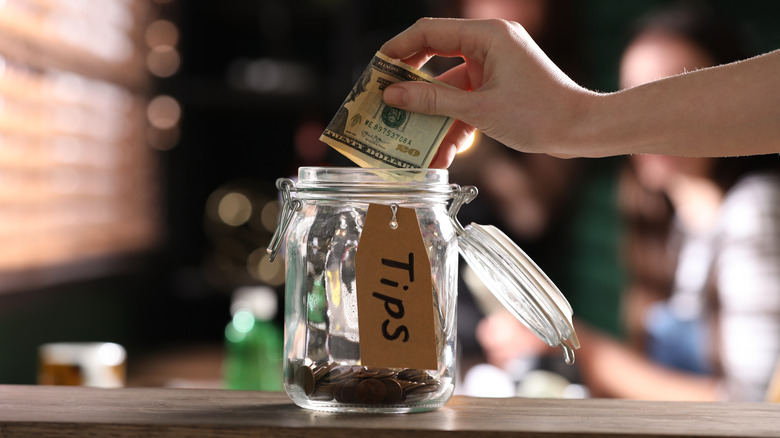 Placing money in glass tip jar 