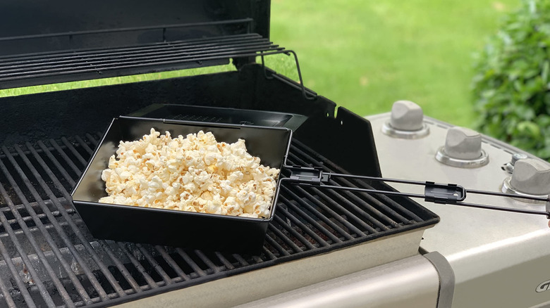 Metal tray with popcorn sitting over barbecue grill.