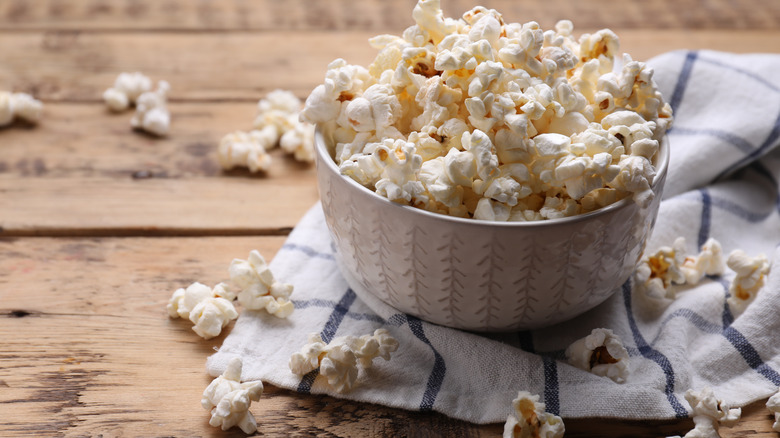 Popcorn in a bowl on a picnic table with dish towel.