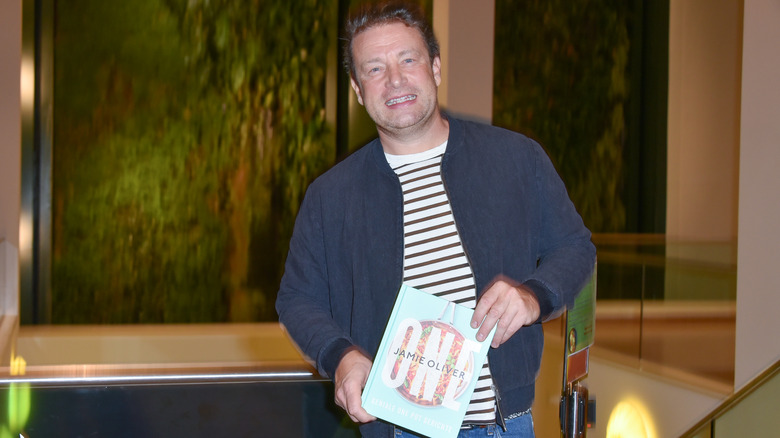 Jamie Oliver holding a copy of his new cookbook One