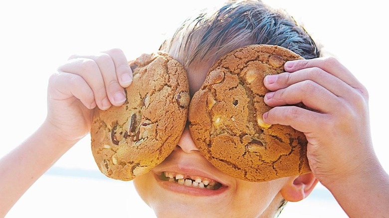 boy holding two cookies over his eyes