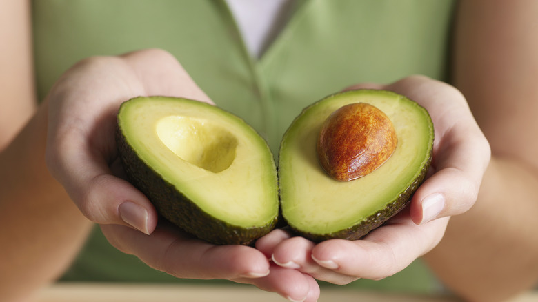 Hands holding avocado cut in half