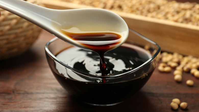 Taking soy sauce with spoon from wooden bowl