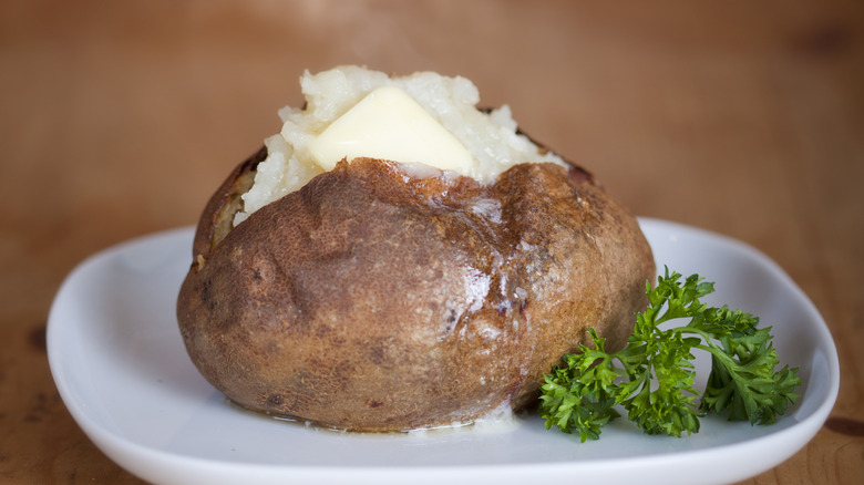 Baked potato with butter on a white plate with parsley garnish