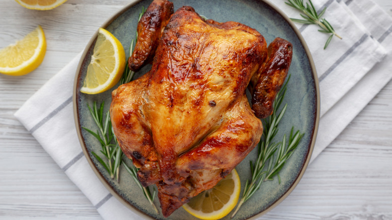 Rotisserie chicken on a plate with rosemary and lemon.