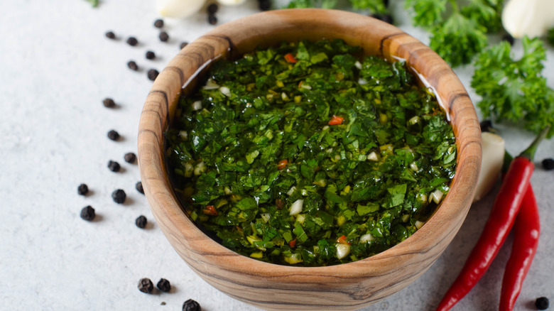 Chimichurri in wooden bowl with red chiles and pepper