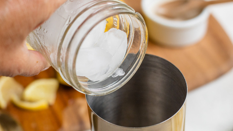 hand pouring ice into cocktail shaker