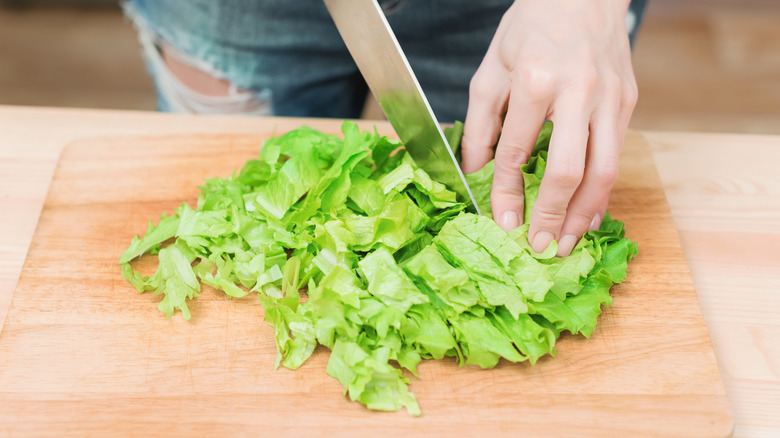 someone cutting lettuce on cutting board