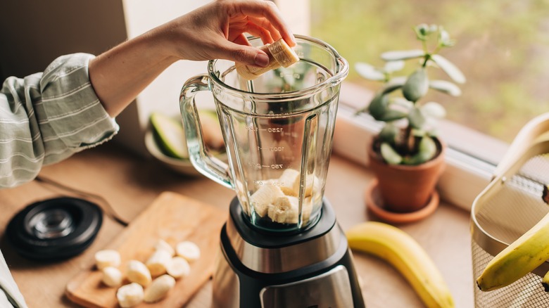 Hand putting banana slices into blender