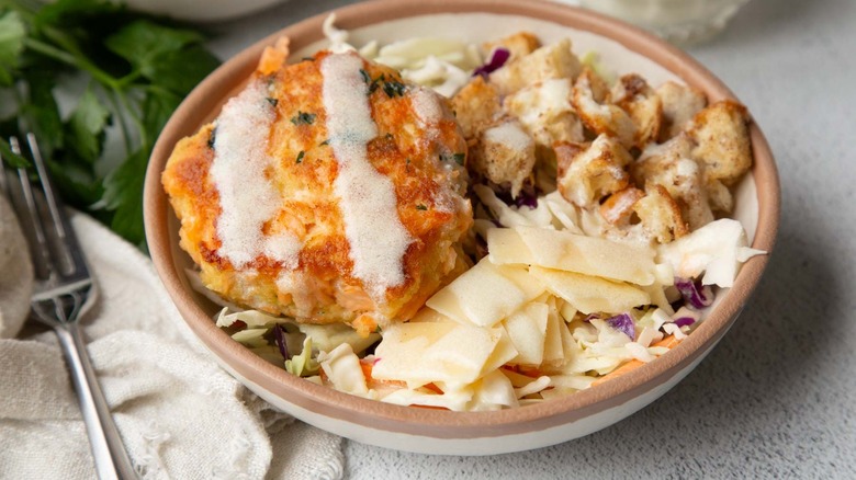 Salmon burger with coleslaw, croutons, and cheese in a beige bowl