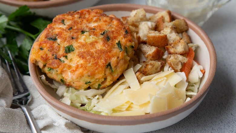 Salmon burger with coleslaw, croutons, and cheese in a beige bowl