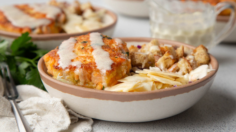 salmon burger with coleslaw, croutons, and cheese in a beige bowl