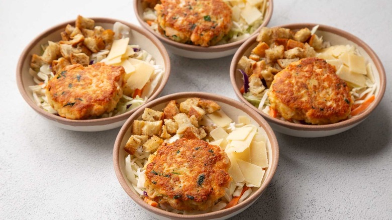 Salmon burgers with coleslaw, croutons, and cheese in four beige bowls