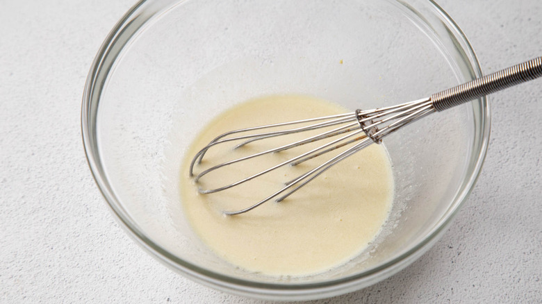 Yellowish-white dressing in a clear bowl with a metal whisk